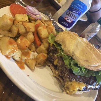 Peppers - A cheeseburger with lettuce, melted cheese, and onions on a bun, accompanied by roasted potatoes with a sauce, on a white plate. - New American Near Me - Page, Arizona