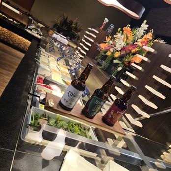 Rodizio Grill - Mesa - 42 item salad bar - A salad bar setup with fresh greens, toppings, and three bottles of beer on a wooden tray, in a restaurant setting with floral decorations. - Steakhouses Near Me - Mesa, Arizona