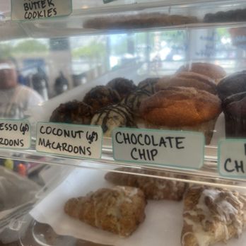 Common Roots - Dessert Case - A glass display case showcases an assortment of cookies and baked goods, including peanut butter cookies, chocolate chip cookies, coconut macaroons, and other items. Handwritten signs label each type of treat, and the background shows a blurred view of the outside environment. The display appears to be part of a bakery or cafe offering a variety of sweet baked goods. - Cafes Near Me - Rye, New Hampshire