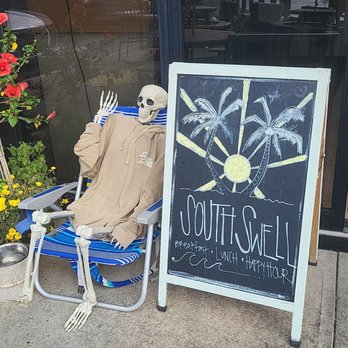 South Swell - a skeleton sitting in a chair next to a sign - Breakfast & Brunch Near Me - West Babylon, New York South Swell - a skeleton sitting in a chair next to a sign - Breakfast & Brunch Near Me - West Babylon, New York
