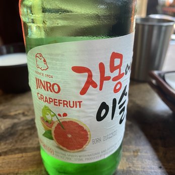 Bul - A green glass bottle of JINRO grapefruit flavored soju, with a label featuring a grapefruit illustration and Korean text, placed on a wooden table. - Korean Near Me - Washington, DC, District of Columbia