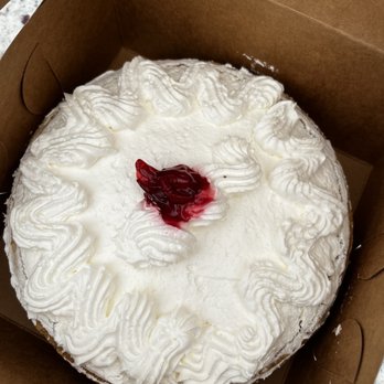 Sergio's Bakery and Cafe - Cherry cream pie - A round cherry cream pie with a whipped cream topping decorated with piped swirls and a cherry topping in the center is placed inside a brown cardboard box. The pie has a crust visible at the edges and is prepared for takeaway or delivery. The whipped cream decoration surrounds the cherry topping, which appears glossy and vibrant. - Bakeries Near Me - Albuquerque, New Mexico