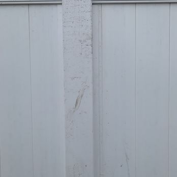 AmeriDream Fence and Deck - A close-up image of a white wooden fence featuring vertical panels and a central vertical post. The fence has some dirt, marks, and minor imperfections, with horizontal trim at the top. The surface appears weathered but intact, with visible grain and slight discoloration. - Fences & Gates Near Me - Joliet, Illinois