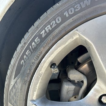 Body Master - A close-up view of a vehicle's tire and rim, displaying tire specifications and a small black and white sensor attached to the rim. The sensor appears to be a tire pressure monitoring device. The tire markings include size and load information, and the rim is metallic with visible brake components behind it. - Body Shops Near Me - Albuquerque, New Mexico