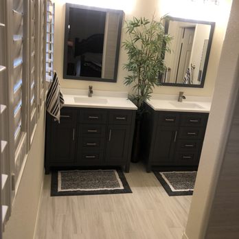 Boonstra Construction, Inc. - two sinks in a bathroom - A bathroom features two dark-colored vanities with white sinks, large mirrors, and towel racks. A tall potted plant is positioned between the vanities. - General Contractors Near Me - Oceanside, California