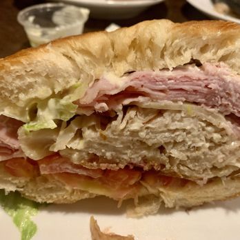 Friar Tuck's - 2nd half of my Club Sandwich! - A detailed view of a club sandwich cut in half, revealing layers of sliced ham, turkey, lettuce, and bread. The sandwich appears freshly made, with visible textures of the bread and fillings. It is served on a plate, with a small container of dipping sauce or dressing in the background. - American Near Me - Manitowoc, Wisconsin