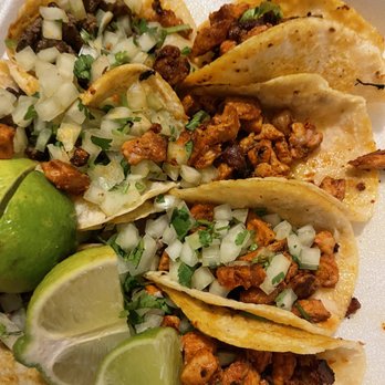 Mad Taco AZ - Tacos. They are a little messed up from the drive but still - A close-up image of four tacos filled with seasoned meat, topped with chopped onions and cilantro. The tacos are arranged on a foam tray, accompanied by lime wedges. The meat appears well-cooked and flavorful, with fresh garnishes adding color and texture. The presentation suggests a casual dining or takeout setting, emphasizing traditional Mexican taco ingredients. - Food Trucks Near Me - Apache Junction, Arizona
