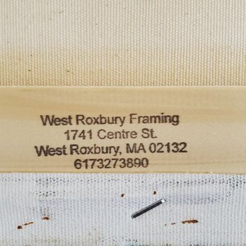 West Roxbury Framing - A close-up photograph of a printed label showing the business name 'West Roxbury Framing,' along with its address at 1741 Centre St, West Roxbury, MA 02132, and a contact number. The label is placed on a textured surface, with part of a canvas or framed item visible below it. The label provides contact details for the framing gallery, which specializes in custom framing services. - Framing Near Me - West Roxbury, Massachusetts