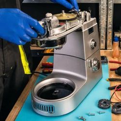 Romano's Appliance Repair - Technician in blue gloves repairing a disassembled espresso machine with various tools on the workbench