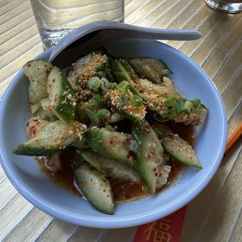 Myers & Chang - Cucumbers - A bowl of cucumber salad garnished with chopped green onions and crushed peanuts, served with a spoon on a wooden table. - Asian Fusion Near Me - Boston, Massachusetts