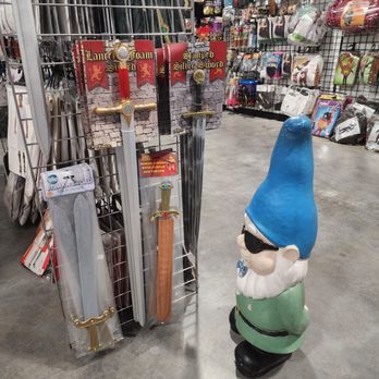 The Costumer - A garden gnome with a blue hat and sunglasses is positioned near a display of toy swords and costume accessories in a retail store. - Costumes Near Me - Schenectady, New York