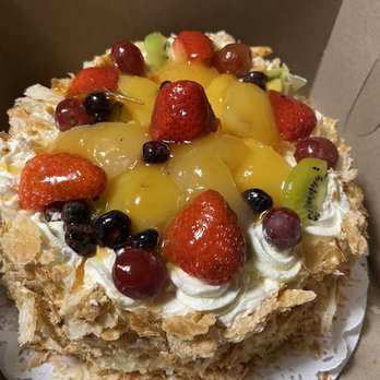 Athens Bakery - My favorite is their Napoleon cake - A cake decorated with various fresh fruits including strawberries, grapes, kiwi, and peaches, placed inside a bakery box. - Bakeries Near Me - Teaneck, New Jersey