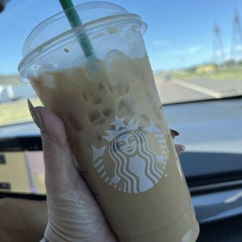 Starbucks - A person holds a Starbucks iced coffee with a green straw inside a car, with a clear sky visible through the windshield. - Coffee & Tea Near Me - Gallup, New Mexico