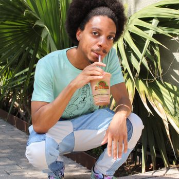 JuiceLand - a young man sitting on the ground with a drink in his hand - Juice Bars & Smoothies Near Me - Dallas, Texas JuiceLand - a young man sitting on the ground with a drink in his hand - Juice Bars & Smoothies Near Me - Dallas, Texas