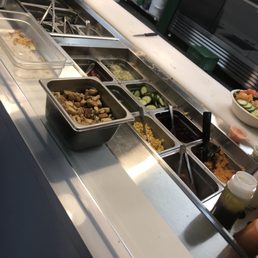 Toppings selection - A salad bar featuring sliced cucumbers, corn, and other toppings in metal containers, with additional ingredients and utensils visible in the background.