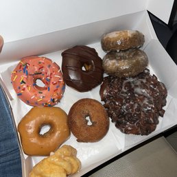 A nice variety of donuts! - A white box contains eight donuts with different flavors, including glazed, chocolate, and frosted varieties, some with sprinkles and toppings.