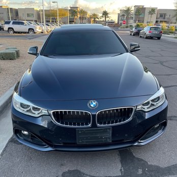 Precision Cut Window Tint - Ceramic Tint on my 428i - A black BMW vehicle with tinted windows is parked in a parking lot near modern residential buildings and palm trees, under a partly cloudy sky. - Car Window Tinting Near Me - Tempe, Arizona