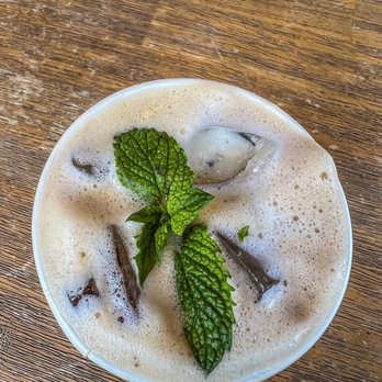 Philz Coffee - Mint Mojito! Oat Milk! ThanX Ariana for the treat! ;) - A mint mojito cocktail with foam, ice, and fresh mint leaves is served in a glass on a wooden table, with a caption thanking Ariana for the treat. - Coffee & Tea Near Me - Berkeley, California