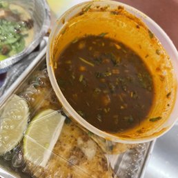 a plastic container filled with soup, tortillas, and lime wedges
