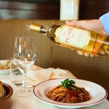 Felice Port Chester - A server pours chilled wine into a glass next to a plate of spaghetti pomodoro garnished with parsley... - Italian Near Me - Port Chester, New York