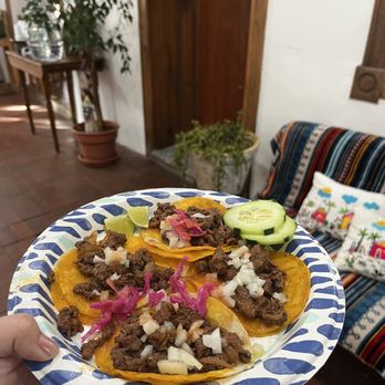 Gobble This - A disposable plate holds tacos with beef, chopped onions, and pickled pink vegetables, garnished with lime wedges and cucumber slices, in a restaurant setting. - Salvadoran Near Me - Albuquerque, New Mexico