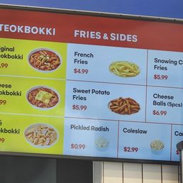 The menu board lists different Tteokbokki dishes such as Original, Cheese, and Rose Tteokbokki, with prices ranging from $16.99 to $18.99. It also offers fried sides including French Fries, Sweet Potato Fries, and Cheese Balls, with prices from $4.99 to $6.99. Additional items like Pickled Radish, Coleslaw, and a Can of Soda are also shown with their respective prices. The board is divided into sections with images of some dishes for visual reference.