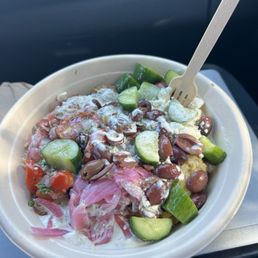 grains bowl with saffron rice, tzatziki and eggplant dip, falafel, corn, onion, tomato and onion, olives, cucumbers, and feta