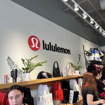 Miromar Outlets - Inside a Lululemon retail store, shopping bags and potted plants are displayed on a wooden counter, with staff assisting customers. - Shopping Centers Near Me - Estero, Florida