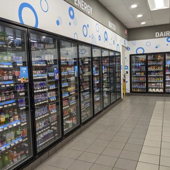 RaceTrac - RaceTrac, Ormond Beach - The image shows an interior aisle of a convenience store with multiple refrigerated glass-door coolers containing beverages and dairy products. The coolers are organized with various drinks and dairy items visible through the glass. The store has tiled flooring and overhead lighting. The wall above the coolers is decorated with signs indicating sections for energy, water, and dairy products. To the right, there are shelves with snack items. The overall setting is clean and well-lit. - Gas Stations Near Me - Ormond Beach, Florida