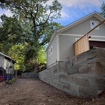 Stone Arch Landscapes - a stone retaining wall and a house in the background - Landscape Architects or Designers Near Me - Minneapolis, Minnesota Stone Arch Landscapes - a stone retaining wall and a house in the background - Landscape Architects or Designers Near Me - Minneapolis, Minnesota