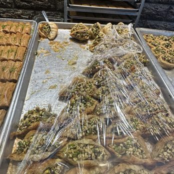 Donya Bakery - Assorted pastries topped with pistachios are displayed on a metal tray, covered with plastic wrap, in a bakery setting. - Bakeries Near Me - Chicago, Illinois