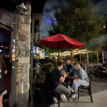 The Brew Inn - a group of people sitting at a table under a red umbrella - Gastropubs Near Me - Brooklyn, New York