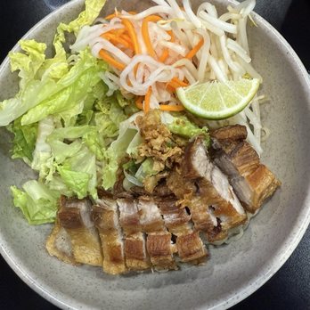 84 Viet - Tom Yum Crispy Pork Belly Dry Noodles - A ceramic bowl holds Vietnamese dry noodles accompanied by crispy pork belly slices, shredded carrots, bean sprouts, lettuce, and a lime wedge. The dish features a variety of fresh vegetables and garnishes, arranged for a traditional presentation of Vietnamese cuisine. - Vietnamese Near Me - Berkeley, California