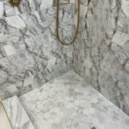 a marble shower - A shower area with marble tiles on the walls and hexagonal marble tiles on the floor, featuring gold fixtures and a drain.