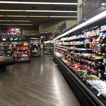 Bashas' - Interior - The image depicts the interior of a grocery store, focusing on a refrigerated aisle with shelves filled with dairy products and packaged foods. The store has a dark wood floor, ceiling lighting, and signage indicating different sections. The background shows additional aisles and product displays, with a clean and organized layout. - Grocery Near Me - Maricopa, Arizona