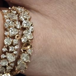 Both engagment ring and wedding ring with missing stones falling out a day apart THIS AFTER WE JUST GOT THE ENGAGMENT RING BACK BEING FIXED! - The image shows a close-up of a diamond ring with multiple stones, some of which are missing, worn on a person's finger. The ring features a gold or similar metal band with numerous clear, faceted stones. The skin of the finger is visible, with natural texture and lines. The background is blurred, focusing on the ring and finger.
