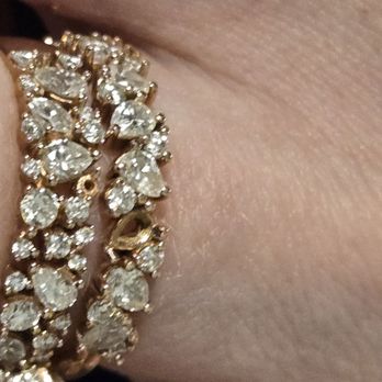Brilliant Earth - Both engagment ring and wedding ring with missing stones falling out a day apart THIS AFTER WE JUST GOT THE ENGAGMENT RING BACK BEING FIXED! - The image shows a close-up of a diamond ring with multiple stones, some of which are missing, worn on a person's finger. The ring features a gold or similar metal band with numerous clear, faceted stones. The skin of the finger is visible, with natural texture and lines. The background is blurred, focusing on the ring and finger. - Jewelry Near Me - Chicago, Illinois