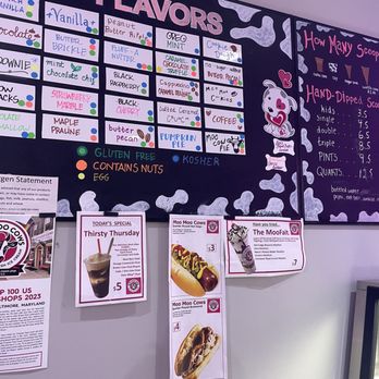 Moo Moo Cows - The image shows a colorful menu board at Moo Moo Cows ice cream shop, listing flavors, toppings, and prices, with additional promotional posters below. - Ice Cream & Frozen Yogurt Near Me - Baltimore, Maryland