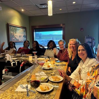 Bonefish Grill - Our group of Travel Agents taking over the bar! - A group of women is sitting at a bar in a restaurant, with drinks and plates of food in front of them, smiling for the camera. - Seafood Near Me - Independence, Ohio