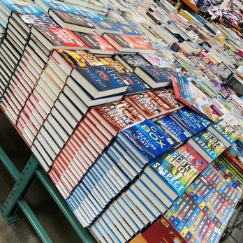 Costco - Books - The image shows a retail store with a table filled with numerous stacks of books. The books include titles related to gaming, adventure, and puzzles, with some featuring colorful covers and bold text. In the background, shelves hold various other products, including clothing and toys, indicating a diverse merchandise selection. The store appears well-organized, with the books prominently displayed for browsing. - Wholesale Stores Near Me - Mount Prospect, Illinois