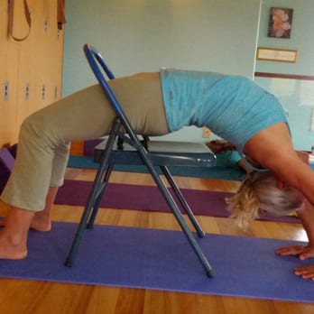 Hilo Yoga - Student utilizes chair prop on mat for support while seeking familiarity with intermediate pose, backbend(wheel). - Yoga Near Me Hilo Yoga - Student utilizes chair prop on mat for support while seeking familiarity with intermediate pose, backbend(wheel). - Yoga Near Me