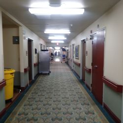 Napa Valley Care Center - West wing: view leading down hall past nurses station leading to therapy room at the left at the end of the hall way