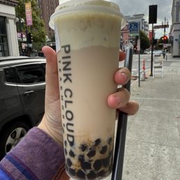 A4. Roasted Oolong Milk Tea - A person holds a large bubble tea from Pink Cloud Tea & More, with tapioca pearls at the bottom, against an urban street background.