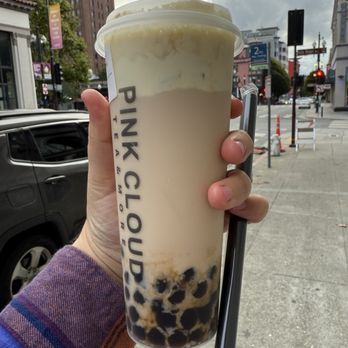 Pink Cloud Tea & More - A4. Roasted Oolong Milk Tea - A person holds a large bubble tea from Pink Cloud Tea & More, with tapioca pearls at the bottom, against an urban street background. - Bubble Tea Near Me - Berkeley, California