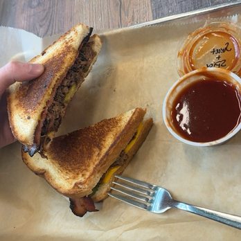 Kiser's Barbeque - Brisket Stuffed Grilled Cheese. It had bacon and pickles on it and the sauce it came with was Amazing! - A grilled cheese sandwich with bacon and pickles is on a tray, accompanied by barbecue sauce and ketchup, with a fork nearby. - Barbeque Near Me - Athens, Ohio
