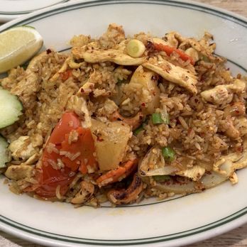 US Thai Cafe - Pineapple fried rice - chicken - hot - A serving of fried rice with shredded chicken, diced vegetables such as tomatoes, onions, and carrots, and seasonings, presented on a white oval plate. The dish is garnished with lemon wedges and cucumber slices, and appears to be a Thai-style fried rice. - Thai Near Me - Edgewater, Colorado