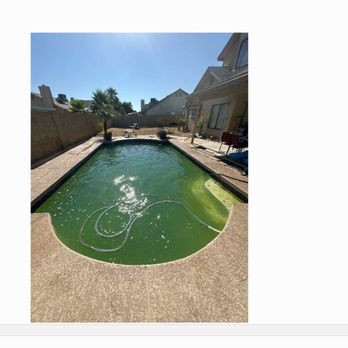 Chuckwalla Pools - A rectangular backyard swimming pool filled with green algae and debris, with a hose inside indicating ongoing cleaning. The pool is surrounded by a concrete deck, with a house and neighboring homes visible in the background under a clear blue sky. The image emphasizes the need for pool maintenance services. - Pool Cleaners Near Me - Goodyear, Arizona