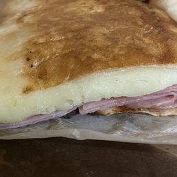 Stromboli - A large stromboli with melted cheese and ham inside, partially wrapped in paper, shown in close-up.