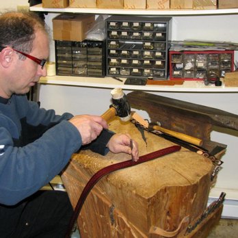 Leathersmith Designs - Jamie using a hole punch tool on tree stump workbench to make adjusting holes in a belt. - Leather Goods Near Me - Dartmouth, Nova Scotia Leathersmith Designs - Jamie using a hole punch tool on tree stump workbench to make adjusting holes in a belt. - Leather Goods Near Me - Dartmouth, Nova Scotia