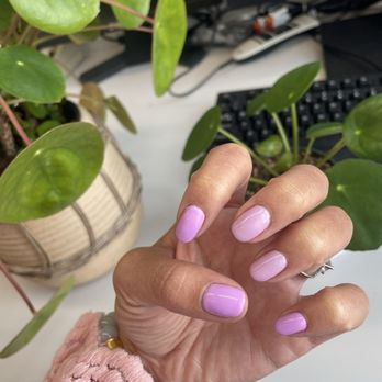 Ruby Nails - Gel manicure (Day 3) - A hand with manicured nails in pastel purple and pink shades is positioned near green houseplants on a desk with computer equipment. - Nail Salons Near Me - Weymouth, Massachusetts